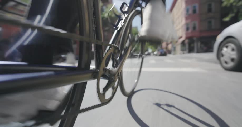 A cyclist pedaling down a city street focusing on the bikes chain and gear while the riders legs move up and down
