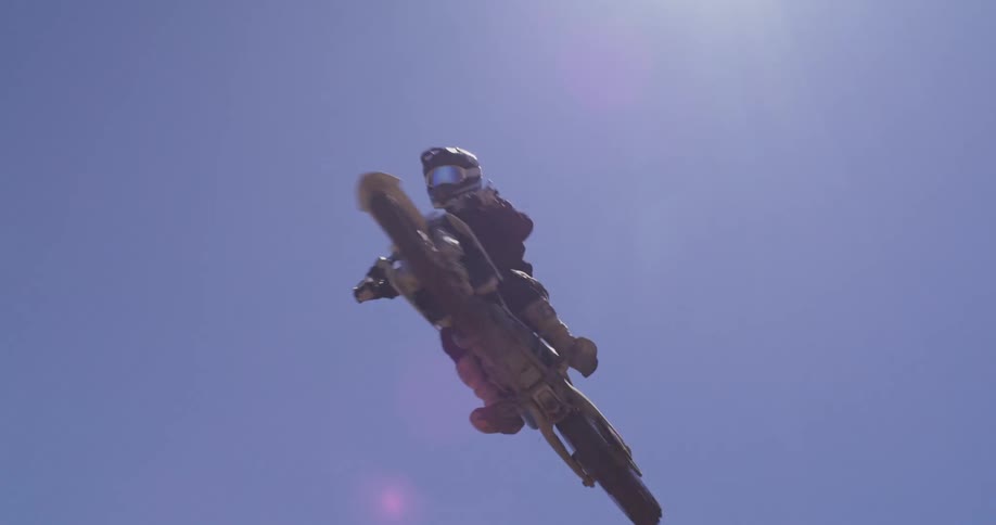 A dirt bike rider soaring through the air performing a daring jump against a backdrop of a clear blue sky