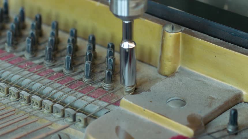 A power tool is being used to loosen a screw in the inner mechanism of a piano breaking a string in the process