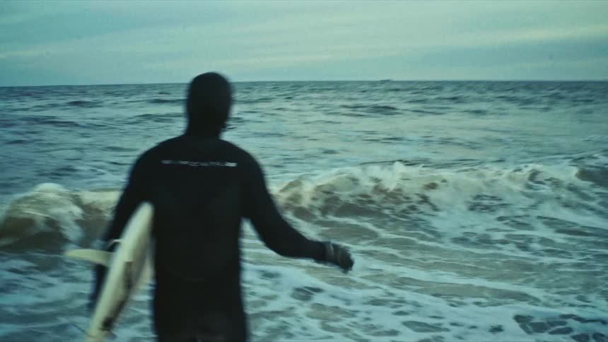 Man wearing a wet suit runs into the surf while carrying a surfboard