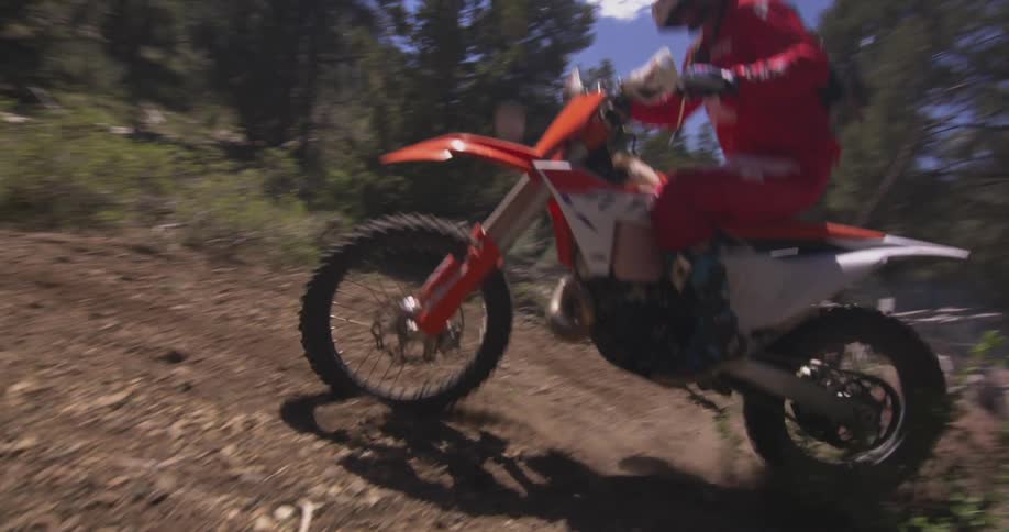 A man is riding a dirt bike on a dirt path that has a log across it