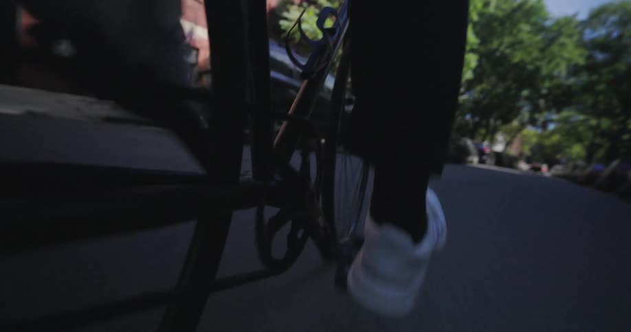 A persons feet are shown pedaling a bicycle down the street in the suburbs