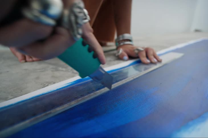 A woman is using a utility knife to cut the edge of a canvas
