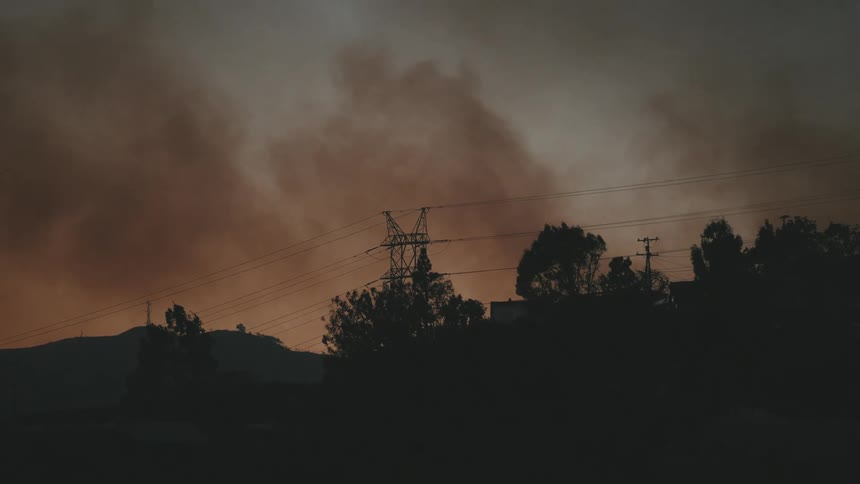 A silhouette of trees and power lines against a smoky orange sky during a fire in the area