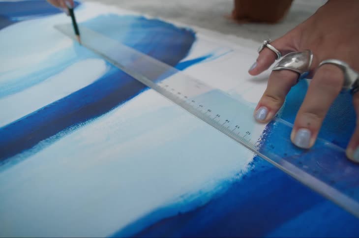 Hand with a ruler and a pencil making a line on the surface of a blue and white paint board