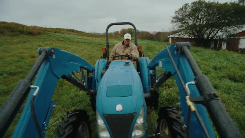 Man in cap driving a blue farm tractor through a field