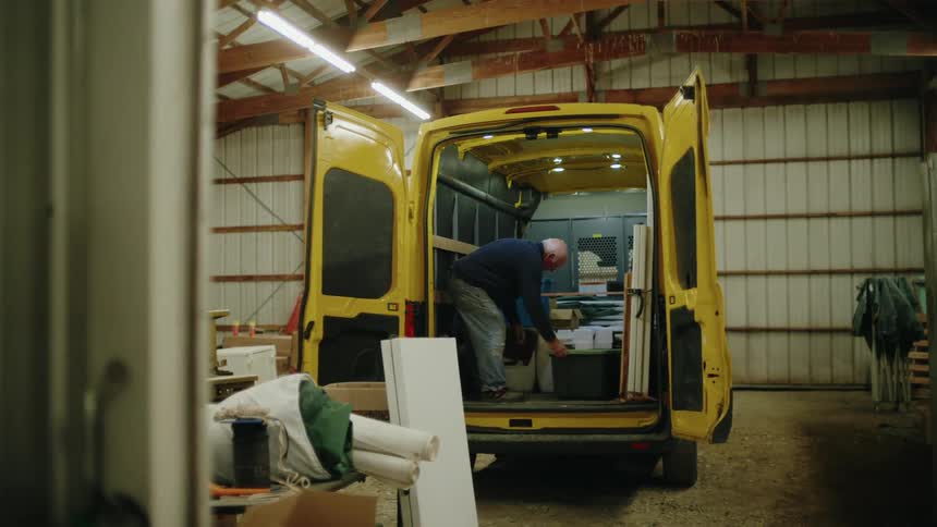 Man organizes materials inside a yellow van parked inside a warehouse