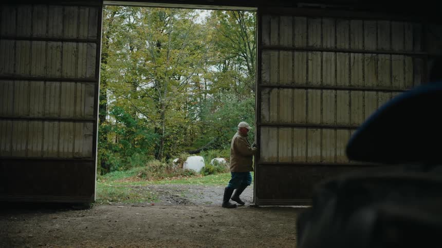A person is pushing open a large sliding door of a barn