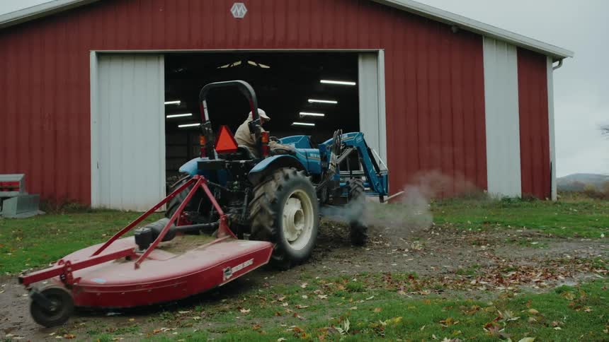 Farmer backs up a tractor out of the barn to deal with fallen leaves