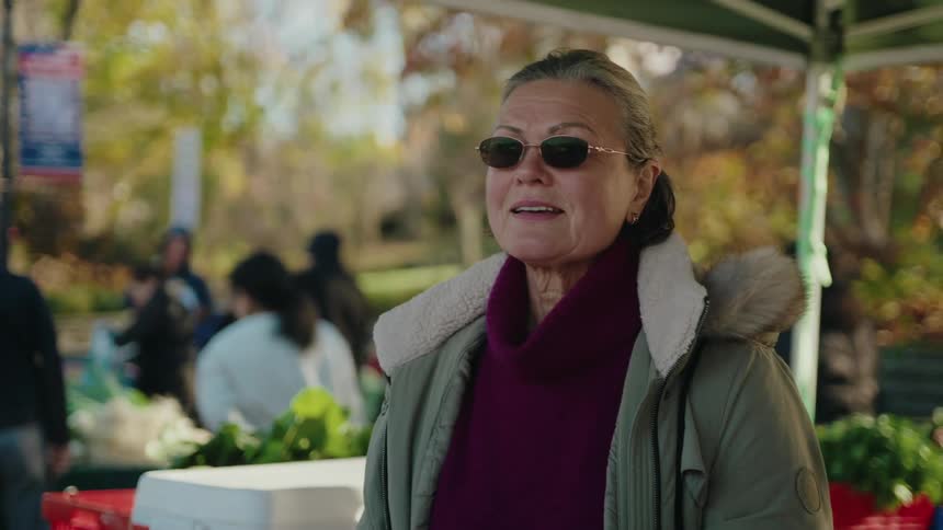 Woman in sunglasses and coat with faux fur collar talking while standing in an outdoor market