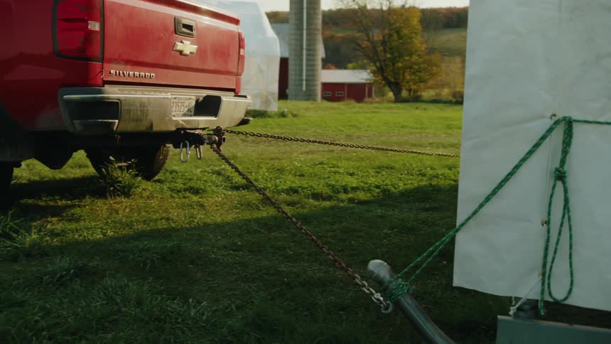 A red pickup truck towing a large metal structure with chains on a grassy field