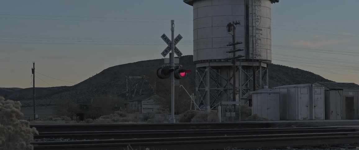 A train crossing signal flashes near a water tower
