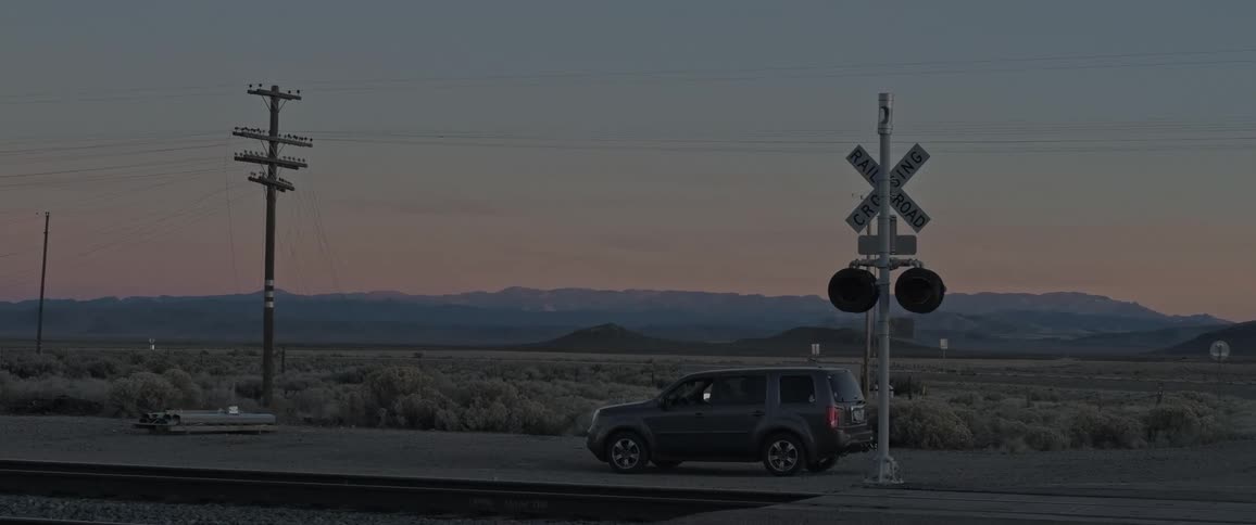 Car parked near a signaled railway crossing with a barren landscape in the background