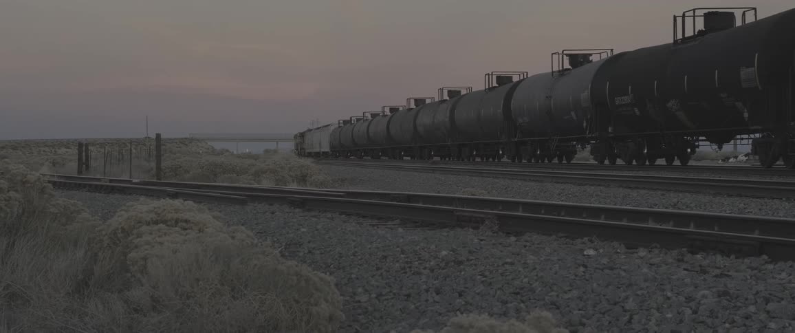 Freight train with tank cars moving on rails in a desert landscape
