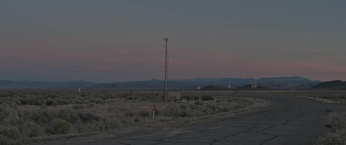 A single utility pole stands tall against a twilight sky next to a desolate winding road