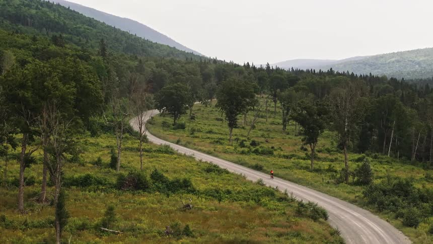Drone shot of a gravel cyclist making their way up a dirt road in the mountains