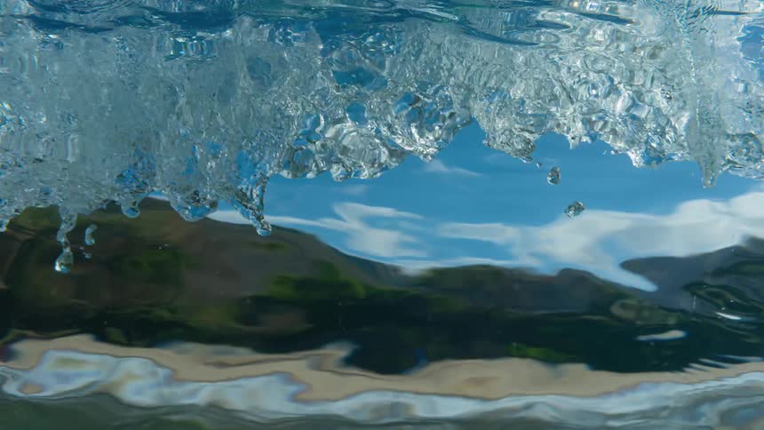 Ocean waves roll near a mountainous coastline on a partly sunny day
