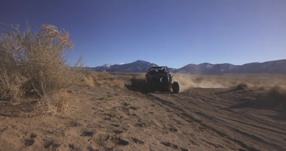 A race car kicks up dust on a desert road under a clear sky