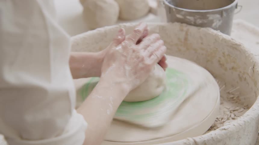 A woman puts water on clay on a pottery wheel as she gets ready to shape it