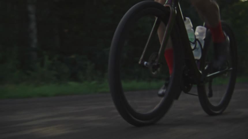 Close up on the wheels of a gravel bike being ridden quickly down a dirt road at sunrise
