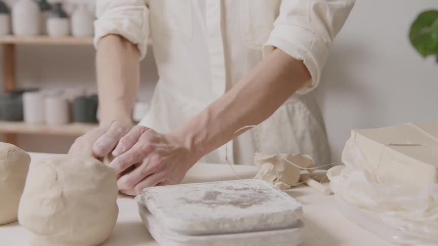 A woman starts kneading a chunk of clay on atable