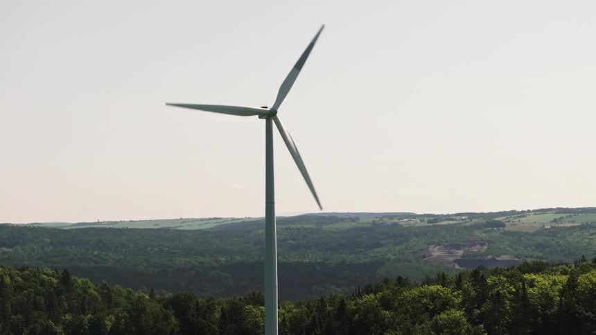 Parallax of a rotating wind turbine standing in a field and towering over the nearby forest