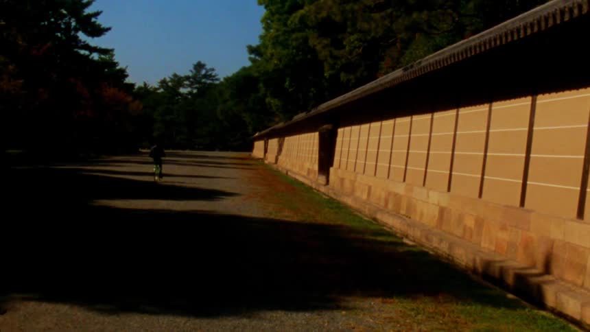A person rides their bike past a stone wall