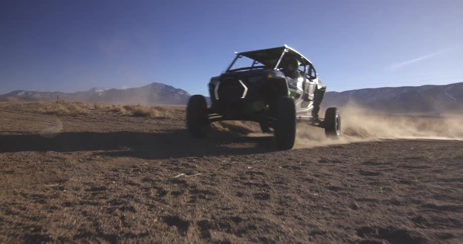 A dune buggy drives through the desert kicking up sand