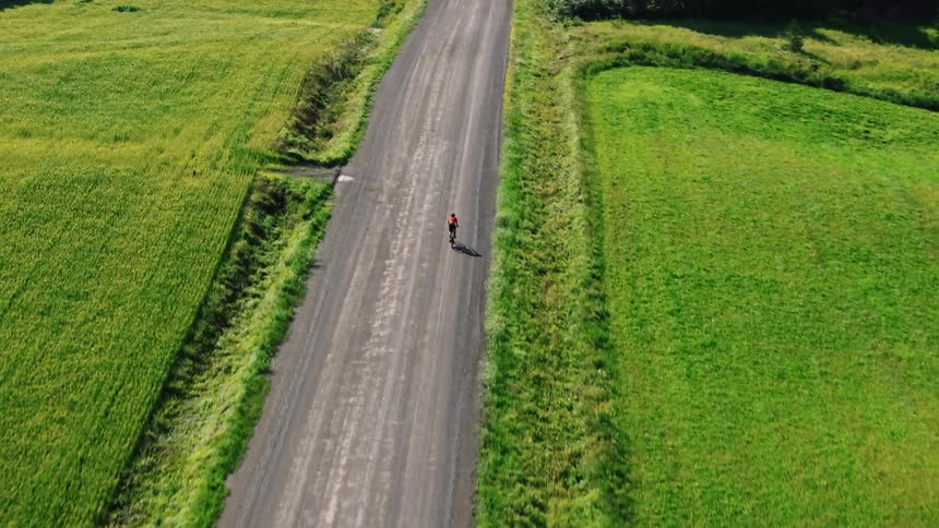 Aerial of a lone gravel cyclist riding on a straight dirt road on a sunny day