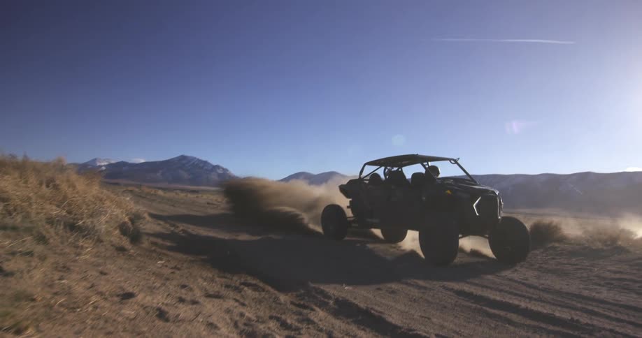 Offroad vehicle in motion raising dust on a dirt track surrounded by dry vegetation