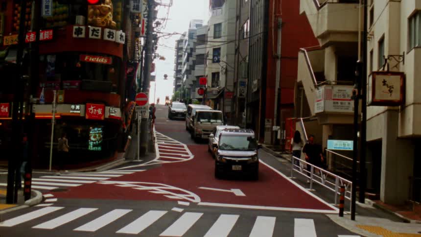 Busy urban street in a commercial area with storefronts lined with signs cars and pedestrians on a paved road