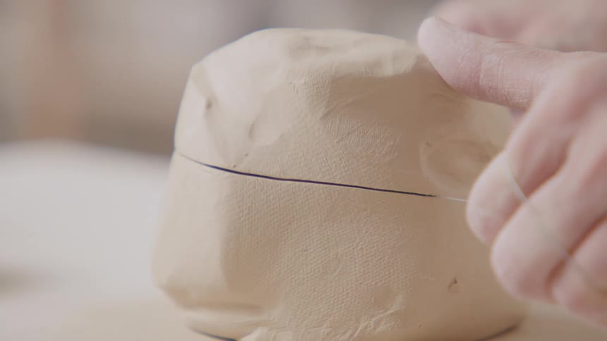 A sculptor uses a wire tool to cut through a piece of clay