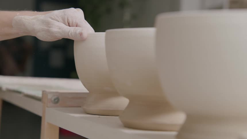 A sculptor places clay bowls on the shelf