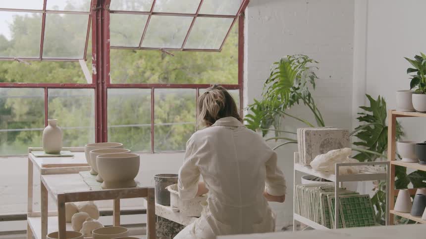 Potter sits working in her workshop with the windows open