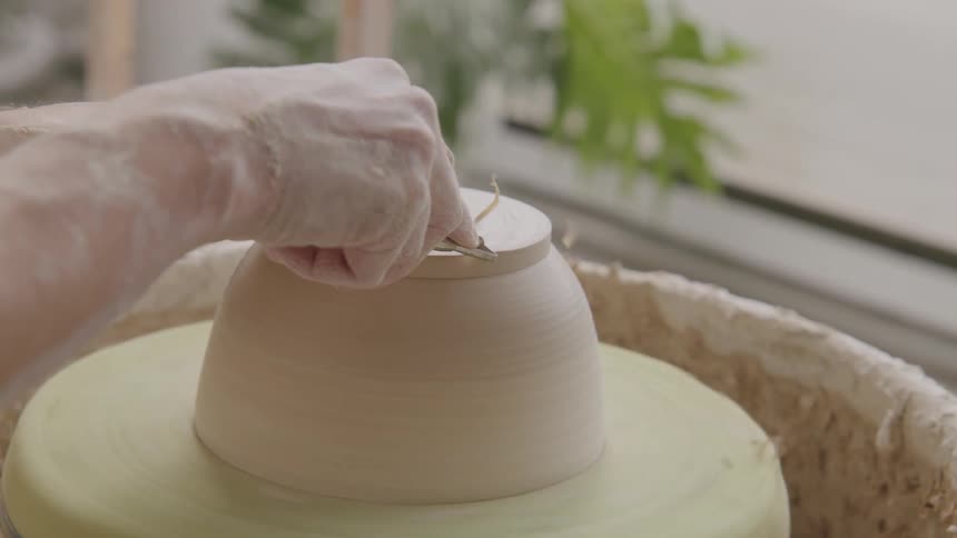 Persons hand shaping a ceramic object on a lathe