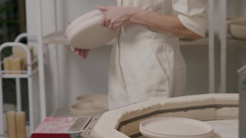 A woman takes plates from a kiln and walks across the room
