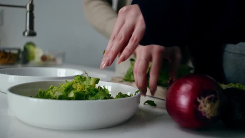 Pair of hands of two people putting chopped salads on a white ceramic plate