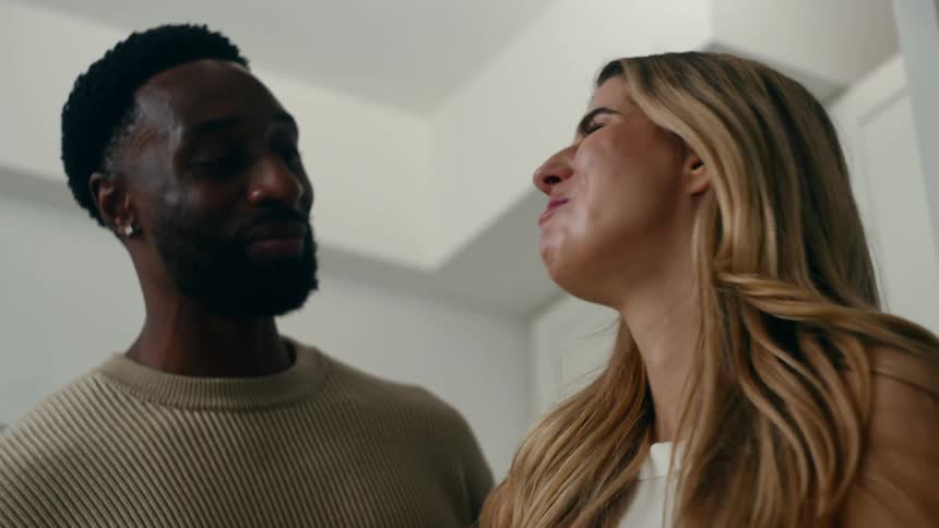 Woman strokes the cheek of her spouse after they taste their food in their kitchen