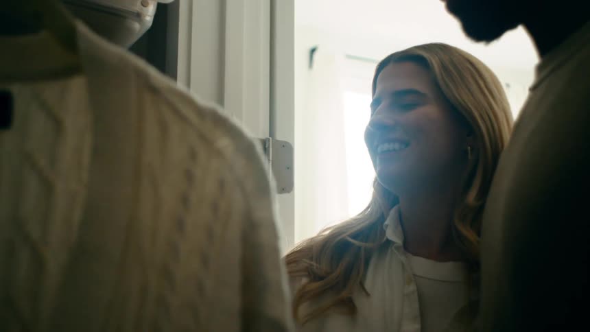 A young couple stands in a closet selecting clothes in a bright well lit room