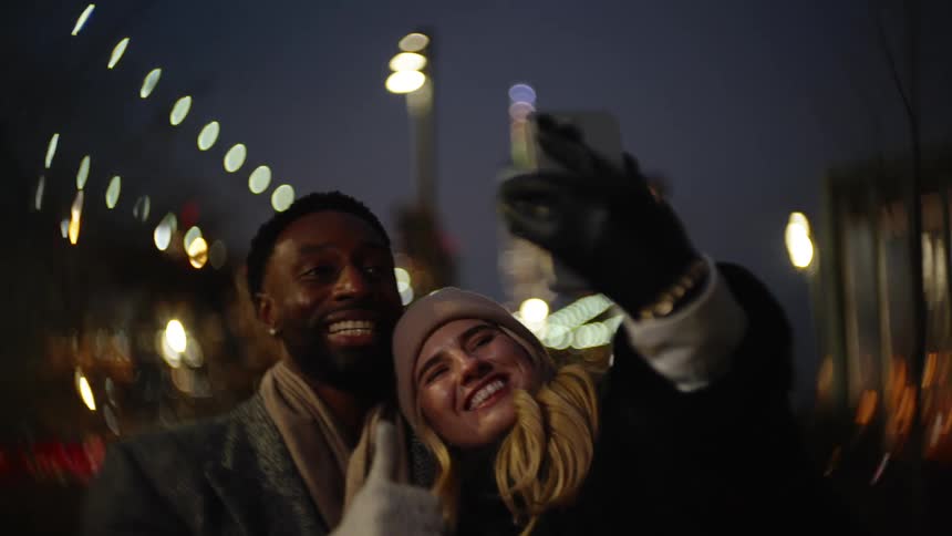 Smiling friends take a selfie while outdoors at night
