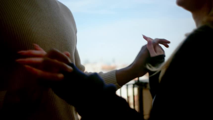 A young couple dances on a balcony holding hands and overlooking the city