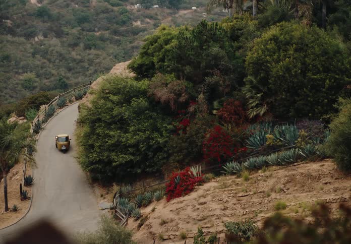 A small yellow vehicle drives along a winding road through a mountainous landscape
