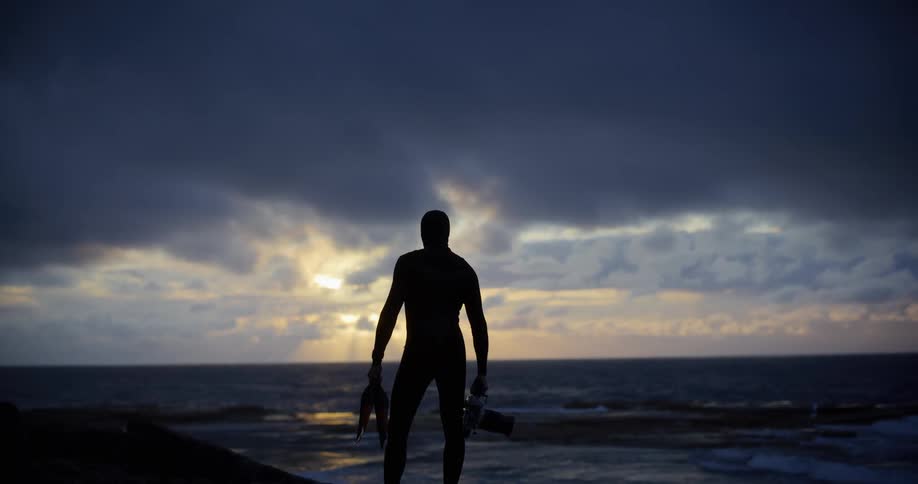 Silhouette of a man in a wetsuit looking at the ocean at sunset