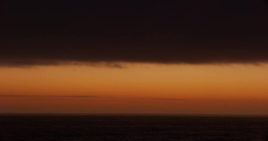 Orange sky at sunset with a dense dark cloud partially covering the horizon over the sea