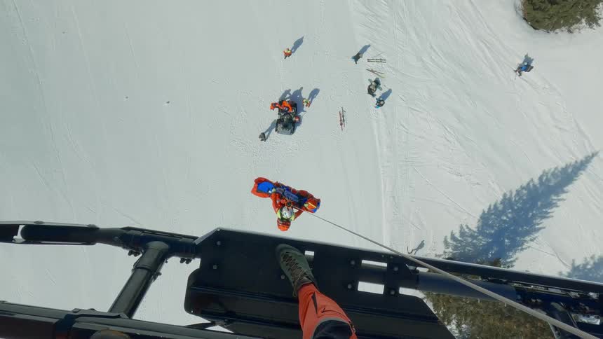A rescue helicopter is lifting an injured person by rope over the mountain
