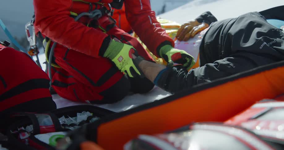 A person in a red rescue suit attends to an injured individual lying on the snow