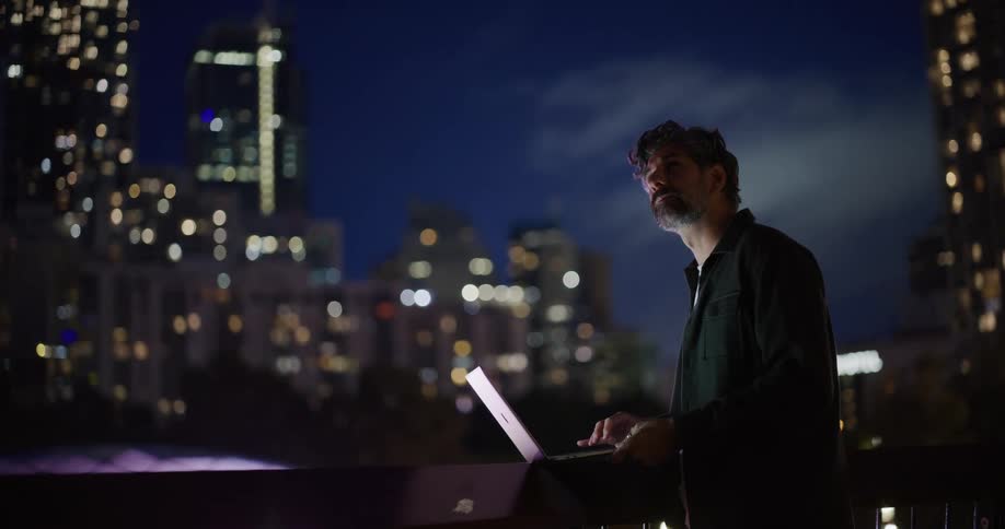 A man using his laptop pauses to look around at the buildings