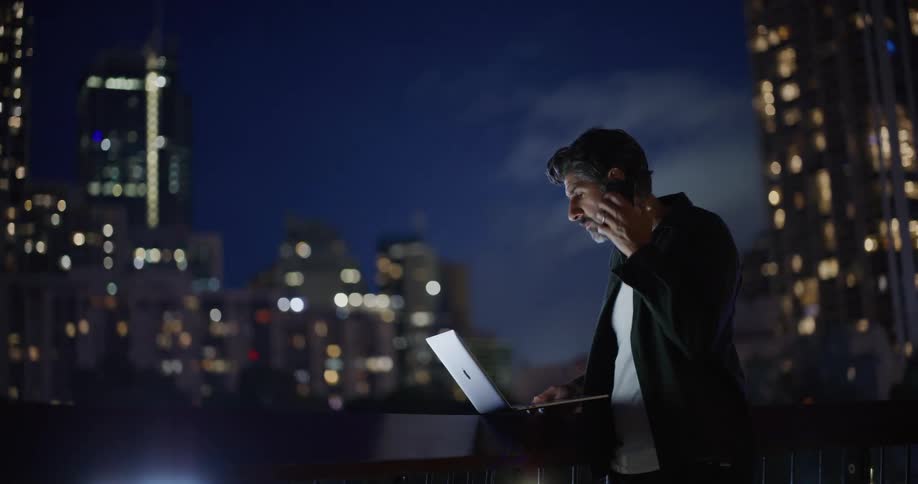 A man talks on his cell phone while using a laptop in the city