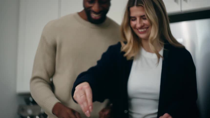 Black man and white blonde woman standing and smiling on a kitchen while they prepare a meal together indoors