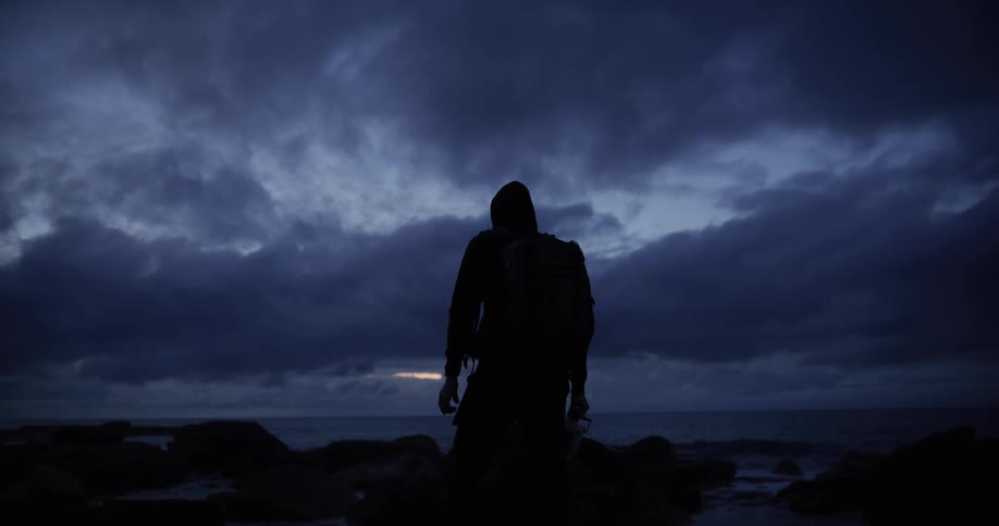 A hiker is looking out over the ocean on a cloudy morning